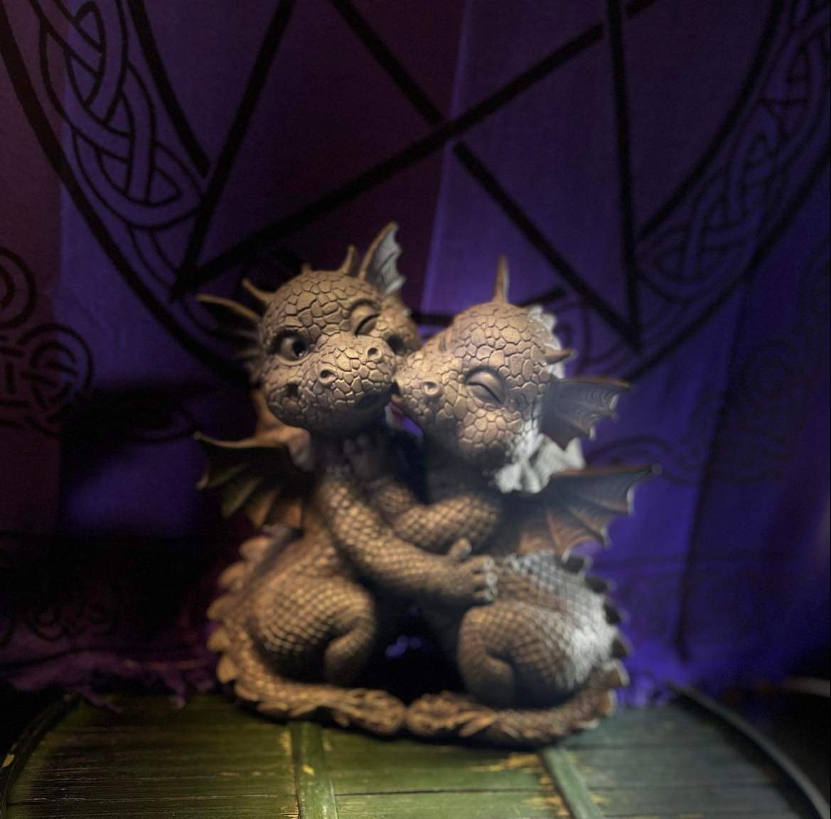 Embracing baby dragon statues against a purple Celtic tapestry